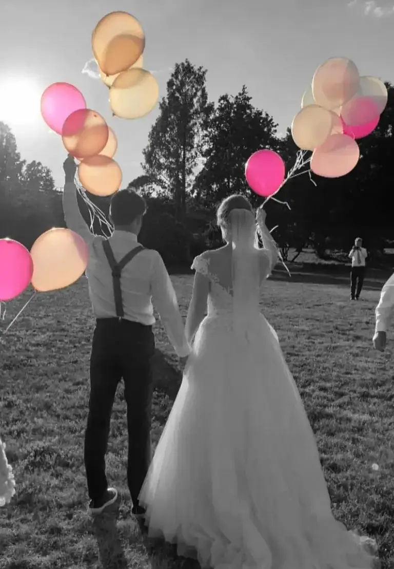 Hochzeitspaar hält bunten Ballons beim Sonnenuntergang auf einer Wiese.