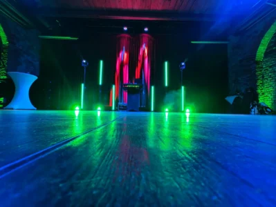 Bunte Lichter und beleuchtete Stangen in einem Eventraum mit Holzboden. Photo by DJ Mirko Anders