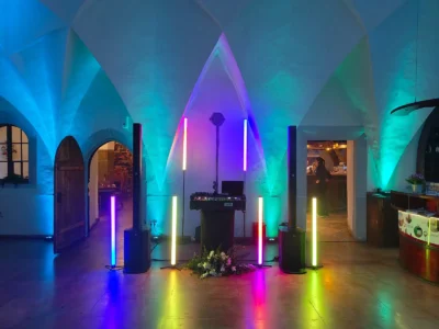 Bunte Lichtinstallation in einem Raum mit Bögen, DJ-Pult und Pflanzenarrangements. Photo by DJ Mirko Anders