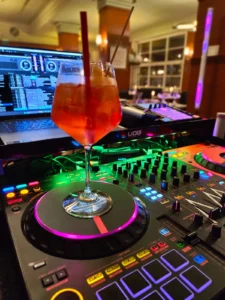 Cocktailglas auf einem DJ-Pult mit bunten Lichtern und einem Laptop im Hintergrund. Photo by DJ Mirko Anders