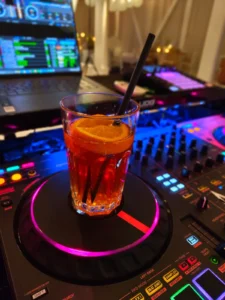 Ein Cocktail mit Orangenstücken auf einem DJ-Pult mit bunten Lichtern. Photo by DJ Mirko Anders