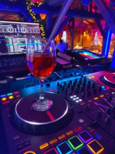 Ein Cocktailglas steht auf einem DJ-Pult mit bunten Lichtern im Hintergrund. Photo by DJ Mirko Anders
