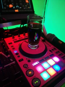 Ein Glas Cola steht auf einem DJ-Deck mit bunten Tasten und Lichtern. Photo by DJ Mirko Anders