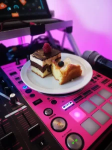 Ein Teller mit Torte und Kuchenschnitten auf einem pinken DJ-Pult. Photo by DJ Mirko Anders