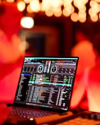 DJ Mirko Anders – Hochzeit Laptop mit DJ-Software, umgeben von warmem, gefiltertem Licht und unscharfen Menschen.